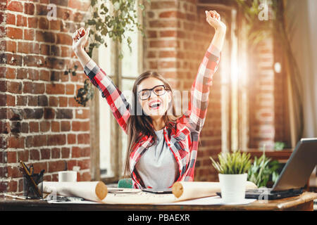 Young pretty long-hair woman architect holding hands up and smiling in the loft modern office Stock Photo