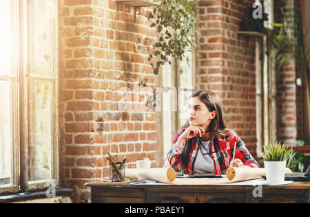 Young pretty long-hair female architect looking to the window and thinking about new project in the loft modern office Stock Photo