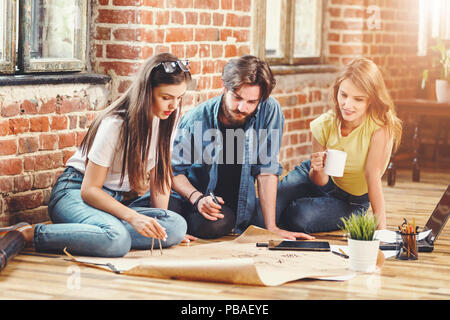 Crew of young professional architects discussing blueprint on the floor in the loft modern office Stock Photo