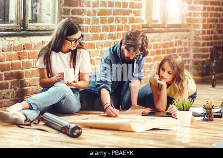 Crew of young professional architects discussing blueprint of new modern house on the floor in the loft light office Stock Photo