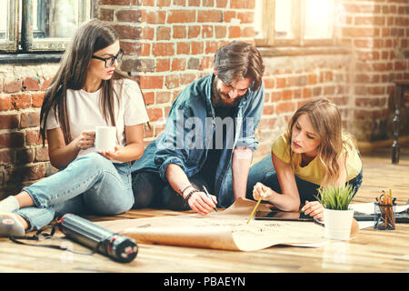 Crew of young professional architects discussing blueprint of new modern house on the floor in the loft light office Stock Photo