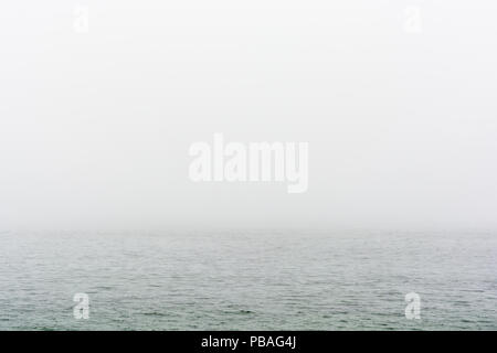 Flat grey sea with wavelets disappearing in the fog. Stock Photo