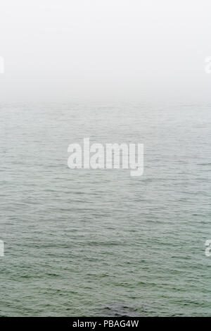 Flat grey sea with wavelets disappearing in the fog. Stock Photo