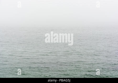 Flat grey sea with wavelets disappearing in the fog. Stock Photo