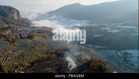 Aerial view on water-filled rice terraces and a valley covered by fog. Yuanyang Rice Terraces early in the morning during spring. Stock Photo