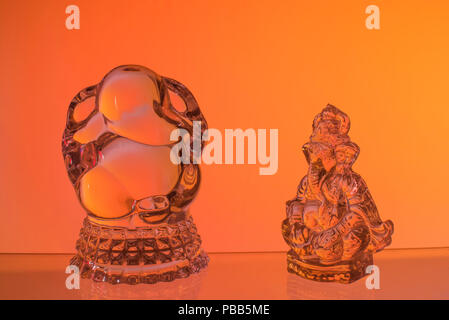 Two idols of Lord Ganesh the divine elephant-headed Hindu Gods made of glass and worshiped by Indian people kept against red orange yellow background Stock Photo