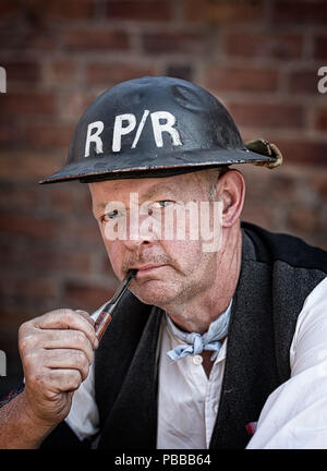 Close-up portrait of wartime re-enactor, in pensive mood, outside in street, wearing helmet & holding pipe to mouth, Black Country Museum 1940s event. Stock Photo