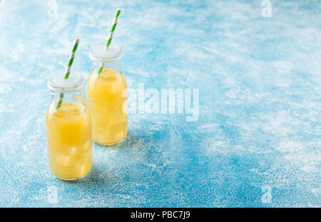 Pineapple cocktail or juice in two glass bottles with straws with ice and two mini pineapples on a blue background Stock Photo