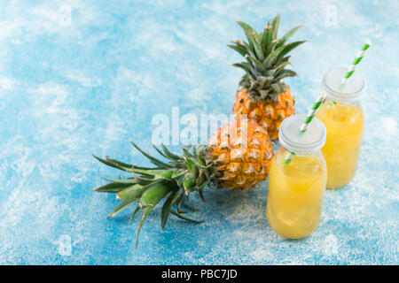 Pineapple cocktail or juice in two glass bottles with straws with ice and two mini pineapples on a blue background Stock Photo