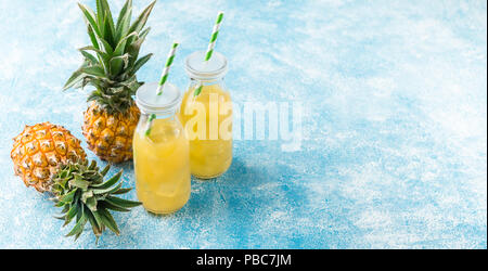 Pineapple cocktail or juice in two glass bottles with straws with ice and two mini pineapples on a blue background Stock Photo