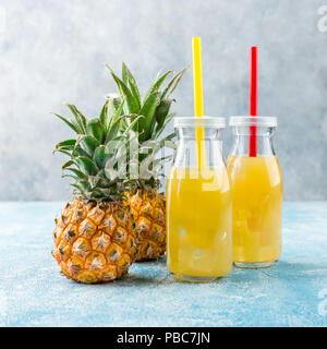 Pineapple cocktail or juice in two glass bottles with straws with ice and two mini pineapples on a blue background Stock Photo