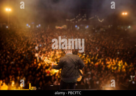 young rock musician on stage playing guitar Young rock musician on stage playing the guitar with the background of all the fans. Stock Photo
