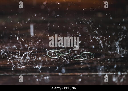 Double white gold wedding rings under water drops splash close up. Studio macro shot on wooden texture Stock Photo