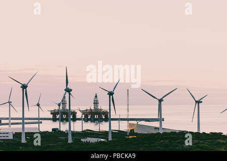 Group of windmills and solar panels for electric power production and oil rigs on coast. Stock Photo