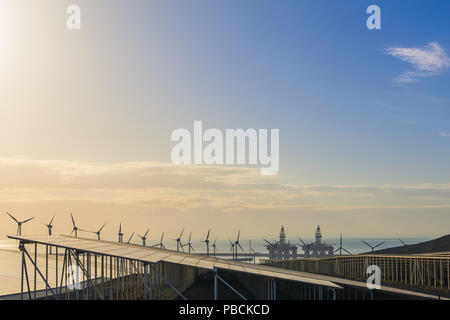 Group of windmills and solar panels for electric power production and oil rigs on coast. Stock Photo