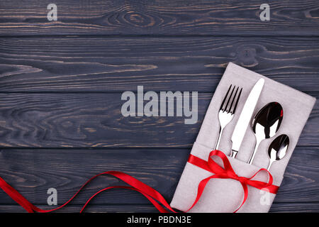 Set of fork, spoon, teaspoon and knife on linen napkin tied with red ribbon on wooden table. Top view. Stock Photo