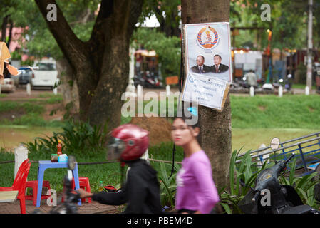 Siem Reap, Cambodia. Saturday, 28th July 2018: A motion blurred young woman stares at the camera with Cambodian general election campaign poster featuring Peoples Party candidates in the background. The polls open on Sunday 29th July. Credit: Nando Machado/Alamy Live News Stock Photo