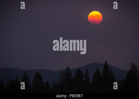 California, USA. 28th June, 2017. Thursday, July 27, 2018.A full moon, ''Blood Moon'' rises over Smith Peak in the Sierra Nevada foothills near Yosemite National Park, California. The sky is choked with smoke from the Ferguson Fire burning nearby. Credit: Tracy Barbutes/ZUMA Wire/Alamy Live News Stock Photo
