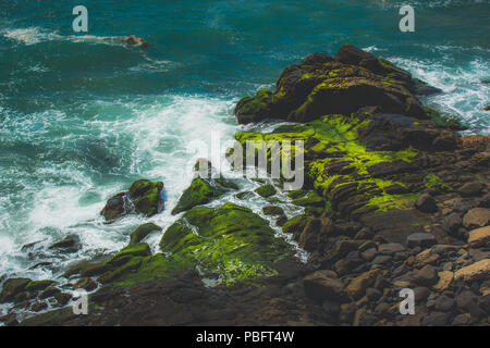 Waves crashing into rock formations covered with green algae, Point Mugu, California Stock Photo