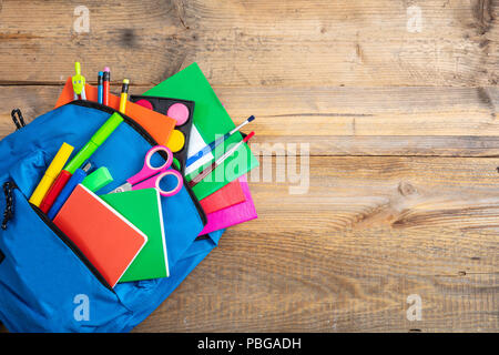 Back to school concept. Blue backpack full of school supplies on wooden background, top view, copy space Stock Photo
