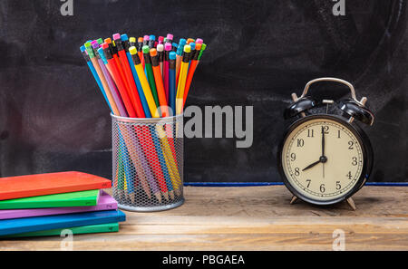 Time for school. School supplies and alarm clock on wooden desk, blackboard background Stock Photo