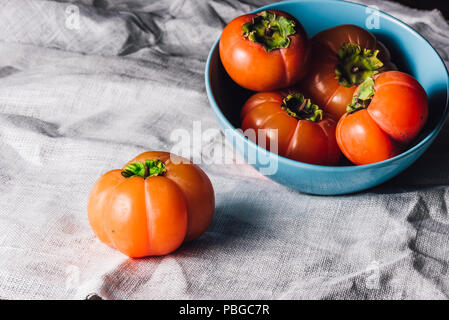 Ripe Persimmons in Blue Bowl Bowl ande One on Table Stock Photo