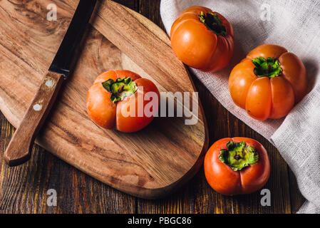 Persimmons with Knife on Wooden Cutting Board Stock Photo
