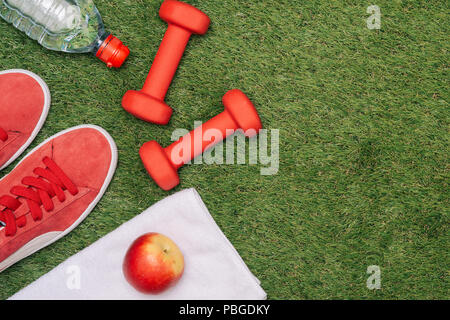 Fitness concept with Exercise Equipment, shoes, apple, Dumbbell and water on green grass. Stock Photo