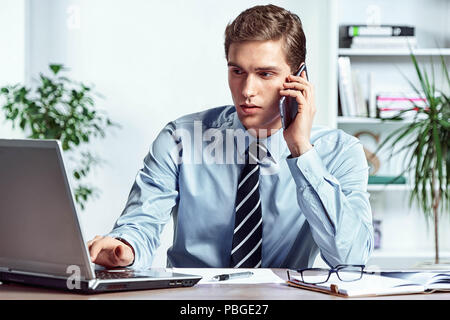 Worker talking on the phone and looks at the laptop. Photo of successful manager working with financial data in the office. Business concept Stock Photo