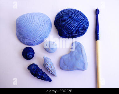 Summer vacation memories concept. Seashells and stone pebbles in shape of heart painted in light and dark blue color and brush with blue color on it.  Stock Photo