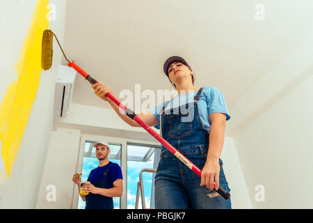 Couple decorating room using paint rollers and paintbrush on wall Stock Photo