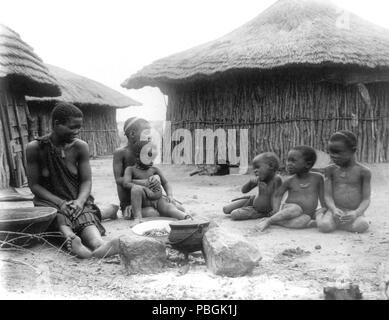 Native woman and five children in front of huts near Bulawayo, Rhodesia, Africa 1890-1925 Stock Photo