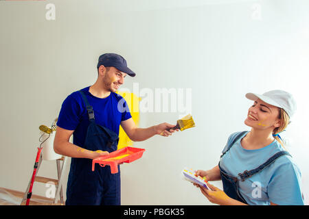 Couple decorating room using paint rollers and paintbrush on wall Stock Photo