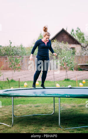 Young White Caucasian Beautiful Plus Size Woman Girl Jumping On Trampoline In Summer Cloudy Day. Stock Photo