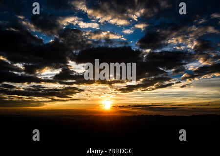 Sunset with orange sun in the center, blue sky and dark couds Stock Photo