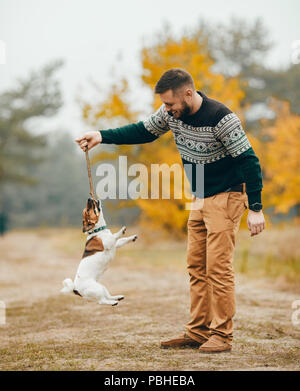 Young man has fun and plays with his dog during walk in autumn forest. Stock Photo
