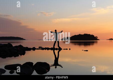 Young man embracing the world in sunset landscape picture with reflections in the water. Stock Photo