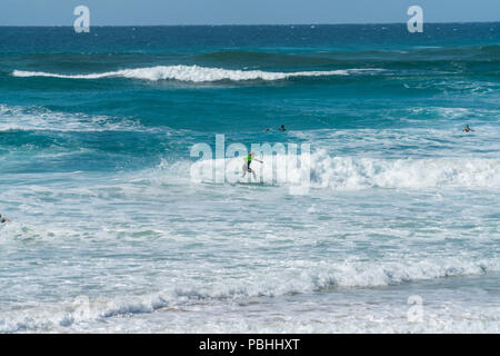 COOLANGATTA, AUSTRALIA - JULY10 2018; Wide surf beach with surfer riding through white wave foam with deep turquoise sea behind