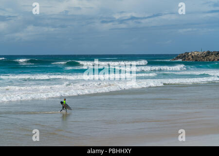 COOLANGATTA, AUSTRALIA - JULY10 2018; Wide surf beach with surfer carrying surfboard along beach in front of surf