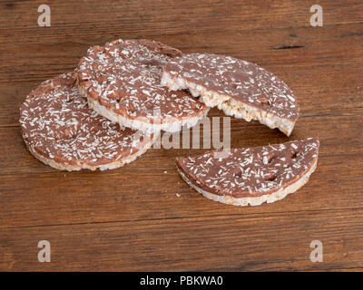 Rice cakes, crackers with milk chocolate and coconut on naturalwood board. Healthy crunchy treat. Stock Photo