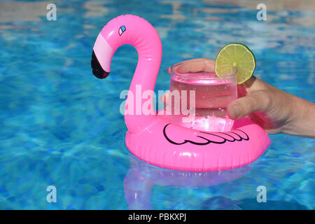 Summer vibes! Woman’s hand, with a cold drink in an inflatable pink flamingo floating drinks holder in a swimming pool Stock Photo