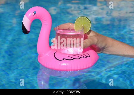 Summer vibes! Woman’s hand, with a cold drink in an inflatable pink flamingo floating drinks holder in a swimming pool Stock Photo