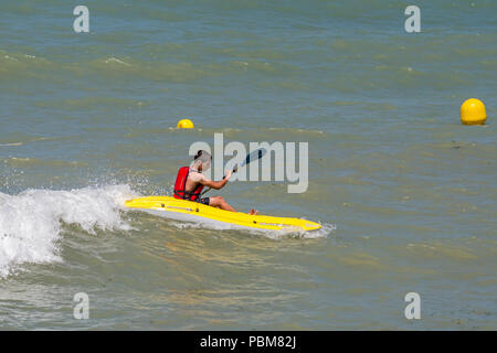 Sportive teenager wearing life-jacket / lifejacket rides wave in kayak at sea in summer Stock Photo