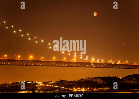 View of the lunar eclipse, the longest blood moon of the 21st century, over the 25th April Bridge in Lisbon, Portugal Stock Photo
