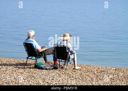 Elderly white couple sitting on the beach at Hastings on a hot summers day, East Sussex England UK Stock Photo