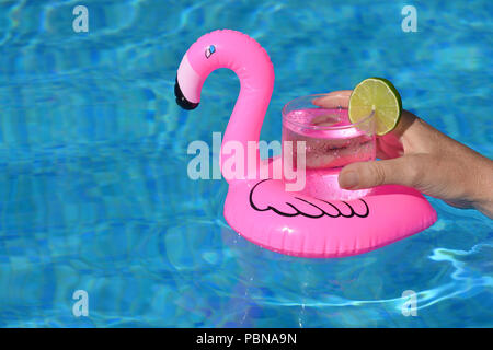 Summer vibes! Woman’s hand, with a cold drink in an inflatable pink flamingo floating drinks holder in a swimming pool Stock Photo