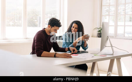 Businesswoman holding a coffee cup looking at her business partner while discussing work sitting at the table in office. Stock Photo