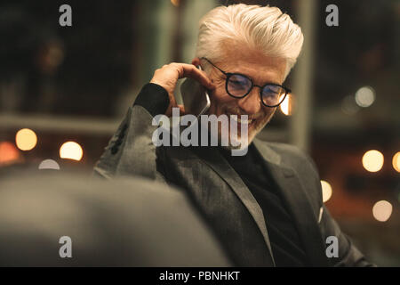 Mature business executive making a phone call and smiling. Caucasian man with eyeglasses talking on mobile phone in office. Stock Photo