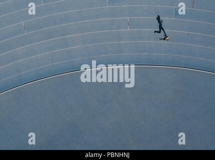 Sprinter running on athletic track. Top view of a sprinter running on race track in a stadium with shadow falling on the side. Stock Photo
