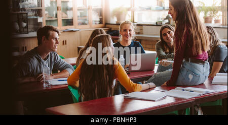 Group of young people sitting in the classroom and talking. University lecture room with students chatting during break. Stock Photo